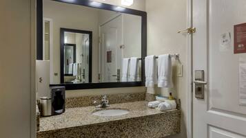 A bathroom with a granite countertop, a sink, a coffee maker, and a mirror.