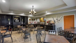 A modern dining area with multiple tables and chairs, a kitchen in the background, and a decorative wall with utensils. - Best Western Plus Searcy Inn (Searcy)