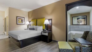 A hotel room with a bed, bedside tables, a chair, a small table, and a bathroom mirror. - Best Western Plus Searcy Inn (Searcy)