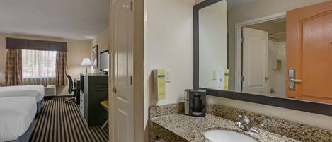 A hotel room with a bed, a desk, a coffee maker, a sink, and a large mirror.