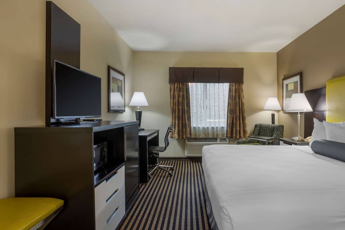 A hotel room with a bed, a desk with a TV, two lamps, a chair, and a window with curtains.