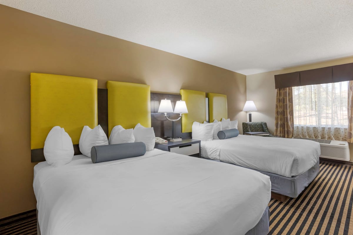 A hotel room with two beds, a large mirror, bedside lamps, a desk, and a window with curtains.