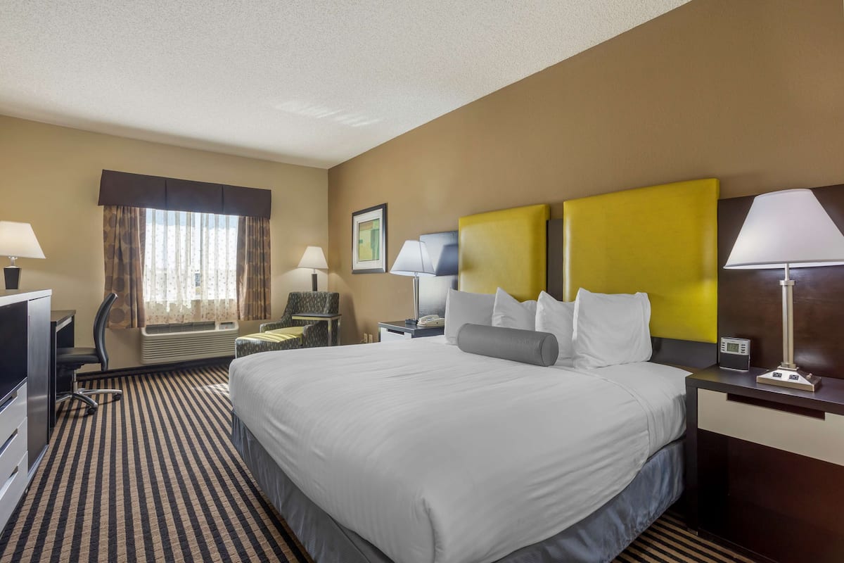 A hotel room with a large bed, two bedside tables with lamps, a desk with a chair, a TV, and a window with curtains.