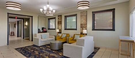 A spacious living area with a large rug, multiple seating options, and a chandelier.