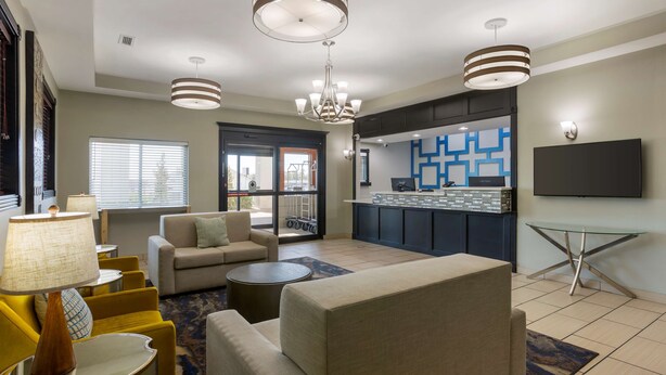 A modern living room with a sofa, armchairs, a coffee table, and a TV. There is a kitchen area with a blue backsplash and a dining table. - Best Western Plus Searcy Inn (Searcy)
