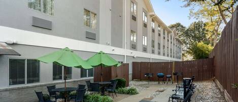 Un patio con mobiliario exterior, incluyendo mesas y sillas, y sombrillas verdes.