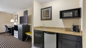 A compact hotel room with a kitchenette, a desk with a chair, a small dining table, and a microwave. - Best Western Plus Searcy Inn (Searcy)