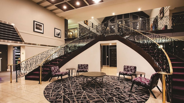 Una gran escalera con barandales de metal ornamentados, un área de descanso circular con un tapiz estampado y una decoración interior moderna.