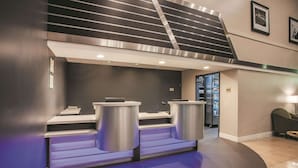 Un área de recepción moderna con mostrador, dos papeleras, una escalera y un refrigerador al fondo.