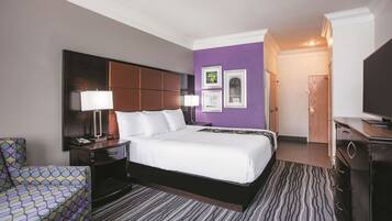 A hotel room with a large bed, a nightstand, a chair, a dresser, and a television.