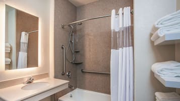 A bathroom with a bathtub, a shower with a grab bar, a sink, and a towel rack with folded towels.