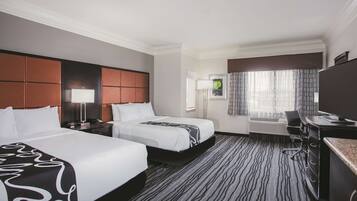 A hotel room with two beds, a desk, a chair, a TV, and a window with curtains.