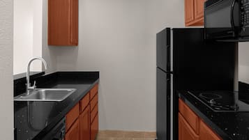 A compact kitchen with a black countertop, stainless steel sink, and wooden cabinets.
