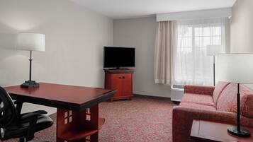 A hotel room with a desk, chair, television, sofa, and two lamps.