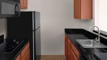 A kitchen with a black refrigerator, a microwave, a sink, and wooden cabinets.