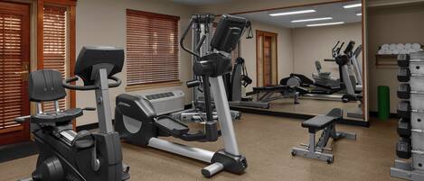A gym with cardio machines, weight benches, and a mirror wall.