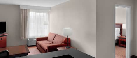 Una habitación de hotel con cama, escritorio, silla, lámpara, televisor y ventana con cortinas.
