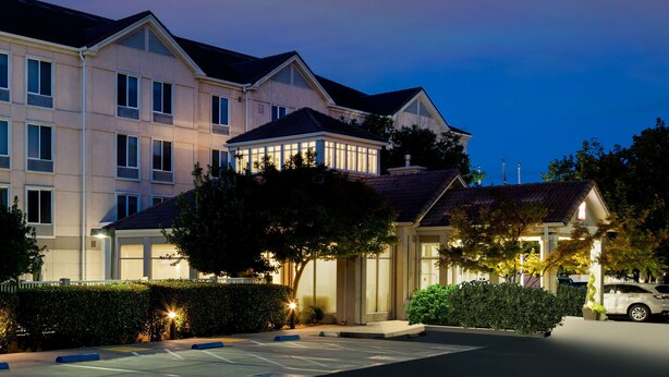 A multi-story hotel with a prominent glass facade, a covered entrance, and a parking area. - Hilton Garden Inn Folsom (Folsom)