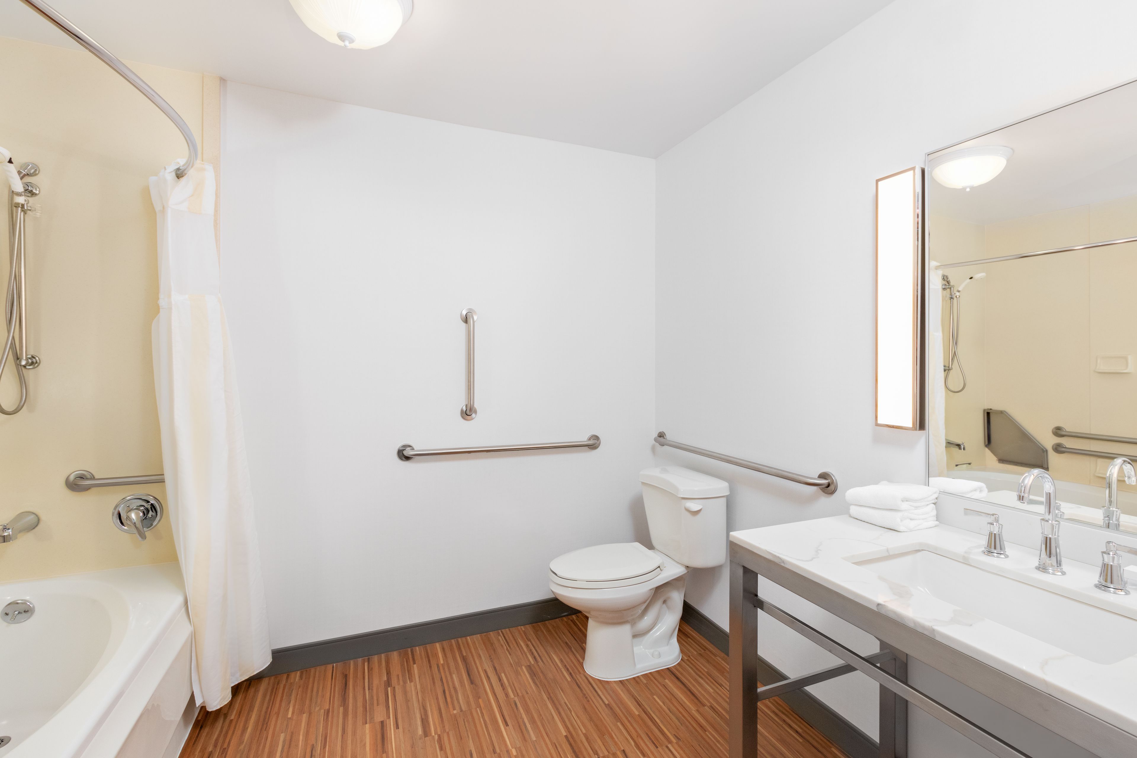 Een moderne badkamer met douche, toilet en wastafel, voorzien van handgrepen en een spiegel.