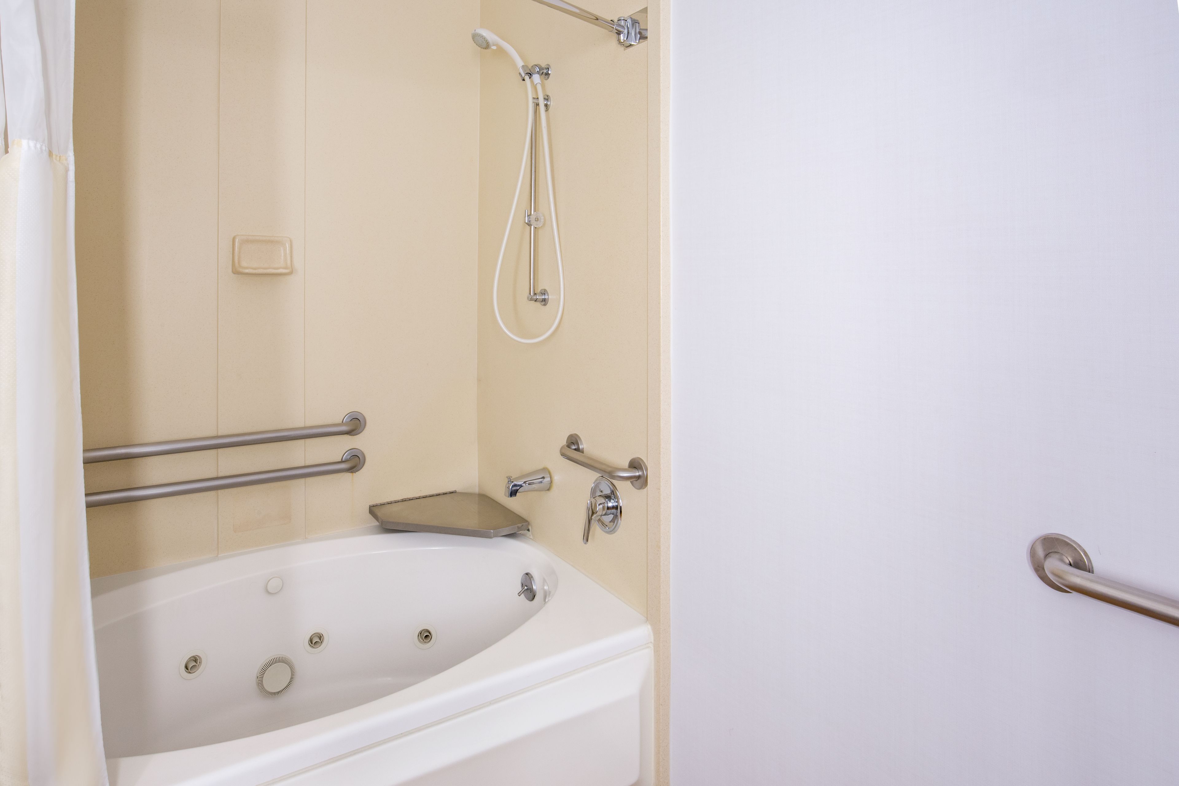 Een badkamer met een bad, douche en toilet. Er zijn veiligheidsbeugels aanwezig.