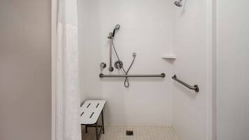 A small, white-walled bathroom with a shower, grab bars, and a white bench.