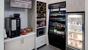 A coffee station with a coffee machine, a refrigerated display case with beverages, and a shelf with snacks and condiments. - Hilton Garden Inn Folsom (Folsom)