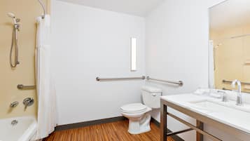 A bathroom with a white toilet, a sink with a mirror, a shower with a curtain, and a wooden floor.