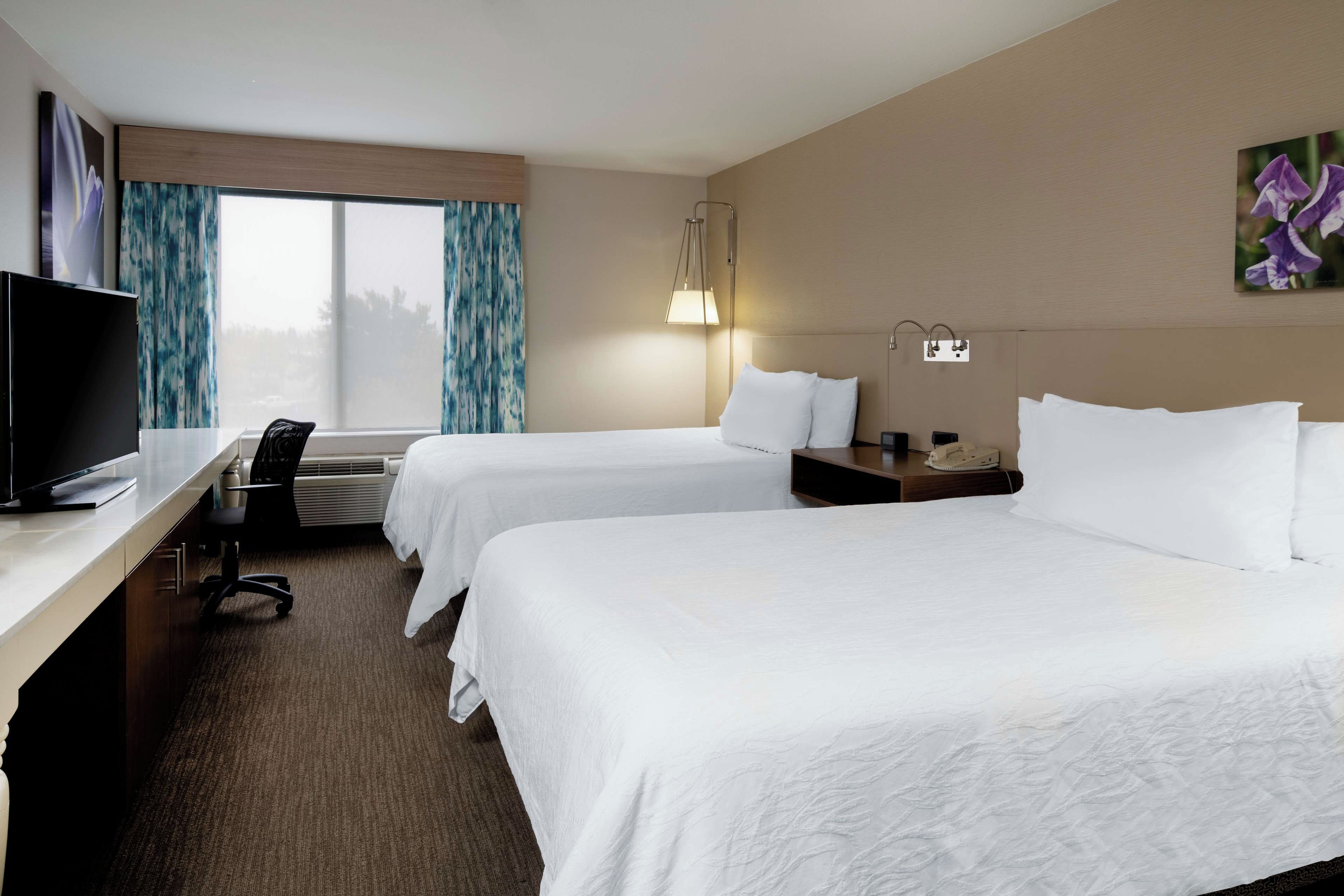 A hotel room with two beds, a desk with a television, and a window with curtains.