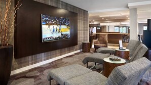 A modern hotel lobby with a large sports game on the wall, comfortable seating, and a view of the dining area. - Courtyard by Marriott Milpitas Silicon Valley (Milpitas)