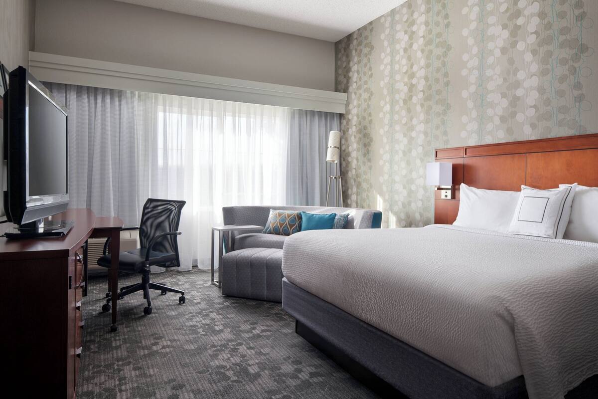 A hotel room with a large bed, a desk with a computer, a chair, and a TV.