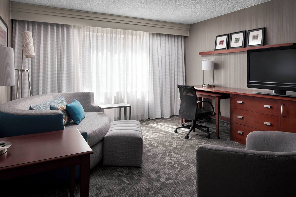 A modern hotel room with a gray sofa, a small desk, a television, and a chair.
