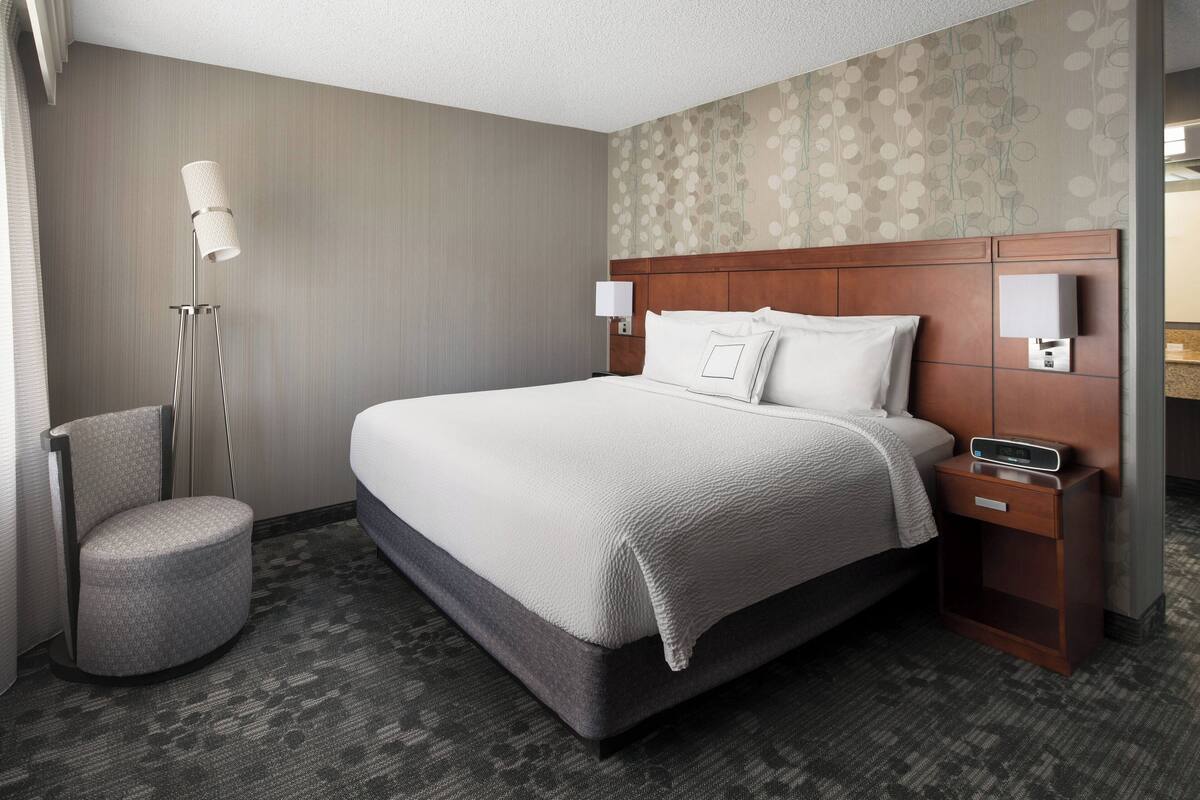 A hotel room with a large bed, a nightstand, a lamp, and a chair.