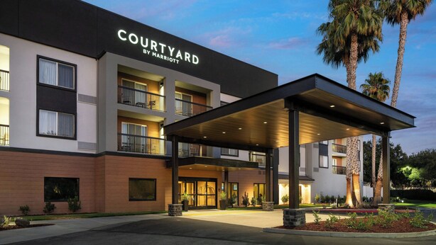 A Courtyard by Marriott hotel with a covered entrance, multiple balconies, and palm trees in the background. - Courtyard by Marriott Milpitas Silicon Valley (Milpitas)