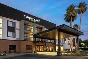 A Courtyard by Marriott hotel with a covered entrance, multiple balconies, and palm trees in the background.