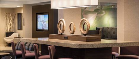 A modern hotel lobby with a reception desk, seating area, and a large screen displaying information.