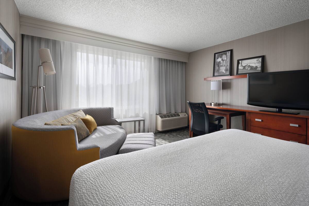 A hotel room with a bed, a sofa, a desk, a television, and a window with curtains.