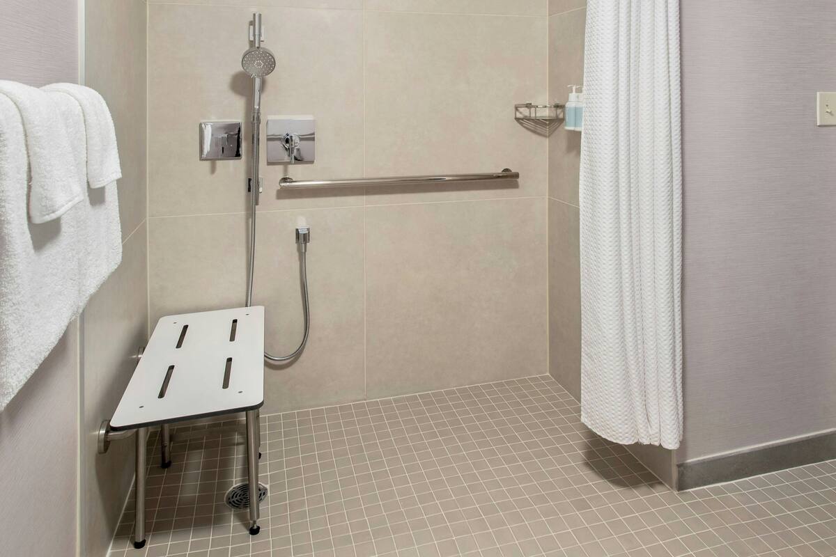 A modern bathroom with a shower, a grab bar, a towel rack, and a small step stool.