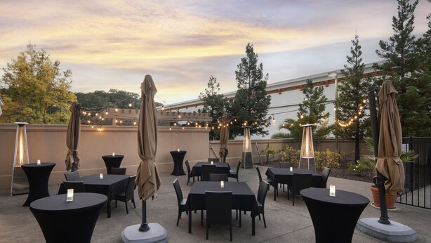 Un espace extérieur aménagé en terrasse, avec des tables et des chaises rondes, des guirlandes lumineuses et des parasols.