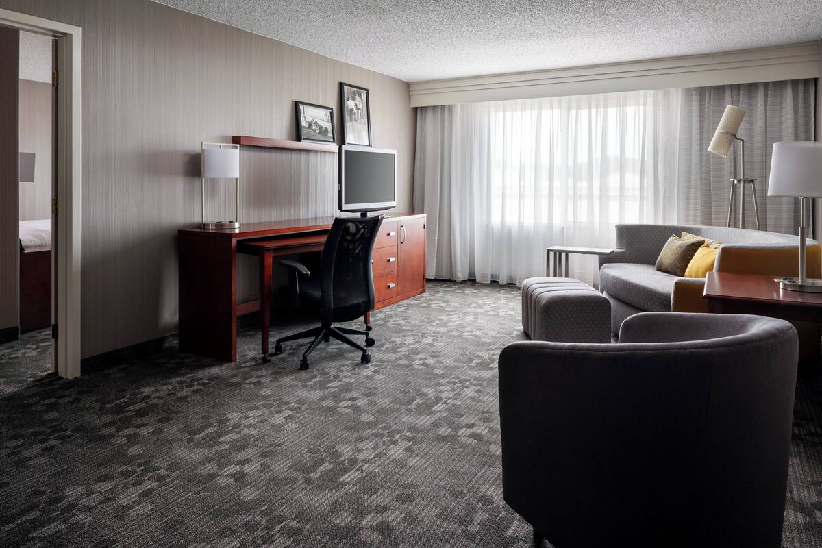 A hotel room with a desk, a chair, a sofa, a lamp, and a television.