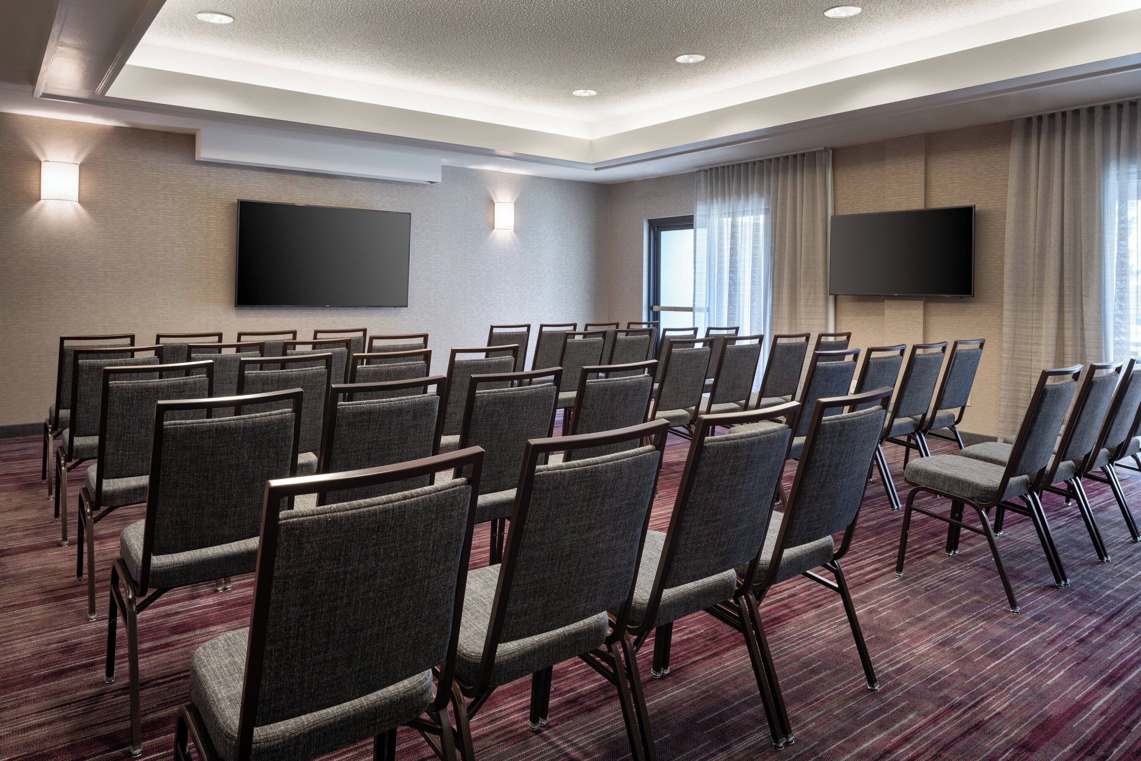 Un salón de conferencias con filas de sillas, un televisor de pantalla plana grande y piso alfombrado.