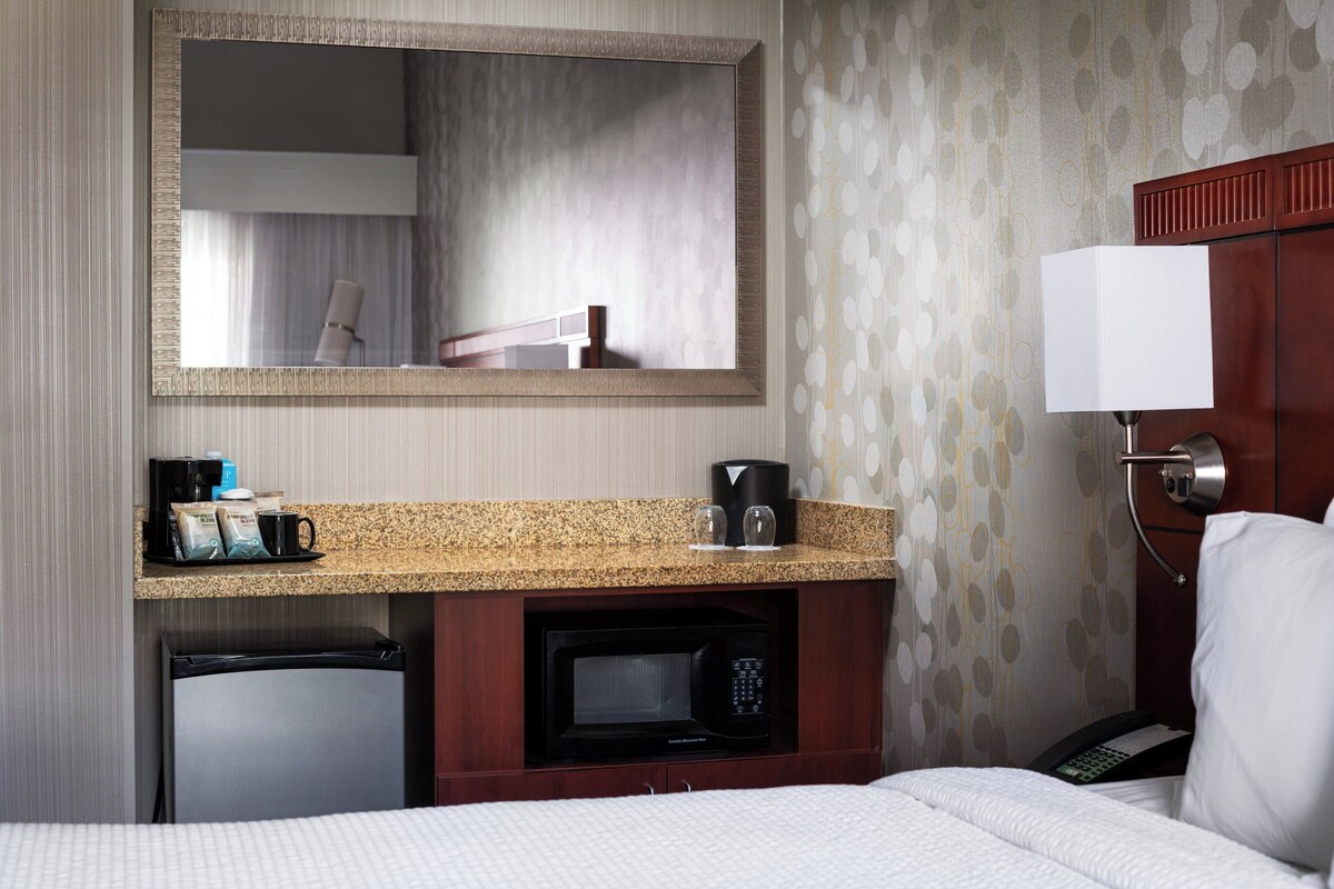 Une chambre d’hôtel équipée d’un lit, d’un bureau avec un micro-ondes, d’une machine à café, d’un téléphone et d’un miroir.