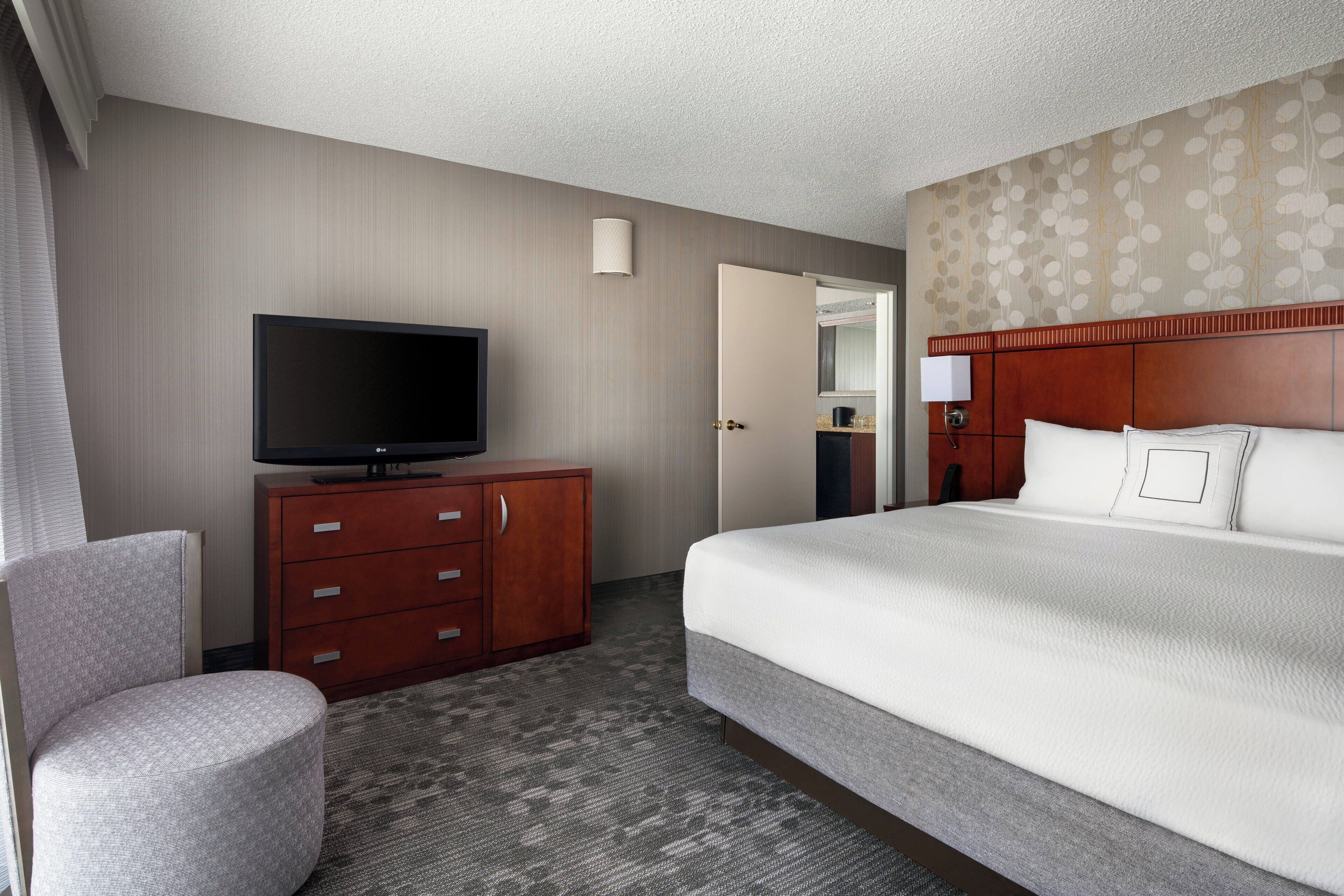 A hotel room with a bed, a television on a wooden cabinet, a chair, and a carpeted floor.