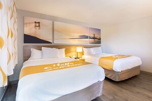 A hotel room with two beds, a nightstand, a lamp, and a view of a bridge.