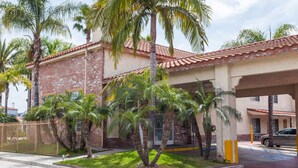 A building with a brick facade, palm trees, and a covered entrance. - Days Inn & Suites by Wyndham South Gate (South Gate)