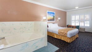 A hotel room with a bathtub, a bed with a gold bedspread, a desk with a chair, and a window with blinds. - Days Inn & Suites by Wyndham South Gate (South Gate)