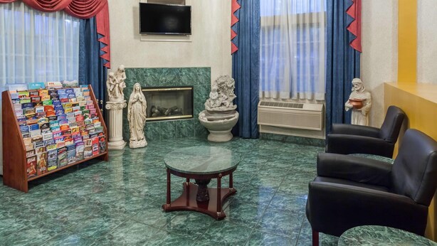 A lobby with a marble floor, a fireplace, a statue, a television, and a display of travel books. - Days Inn & Suites by Wyndham South Gate (South Gate)