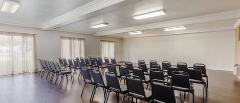 A conference room with rows of chairs, large windows with curtains, and recessed ceiling lights.