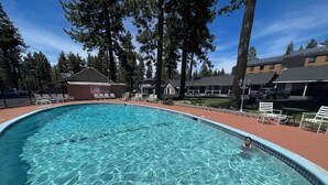 A swimming pool with clear water, surrounded by lounge chairs and a building with a sloped roof. - Tahoe Hacienda Inn (South Lake Tahoe)
