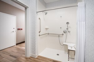 Un baño moderno con ducha a ras de suelo, barra de apoyo, ducha de mano y lavamanos pequeño.