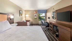 A hotel room with a large bed, a desk with a chair, a television, and a window with a view of greenery. - Hampton Inn Tracy (Tracy)